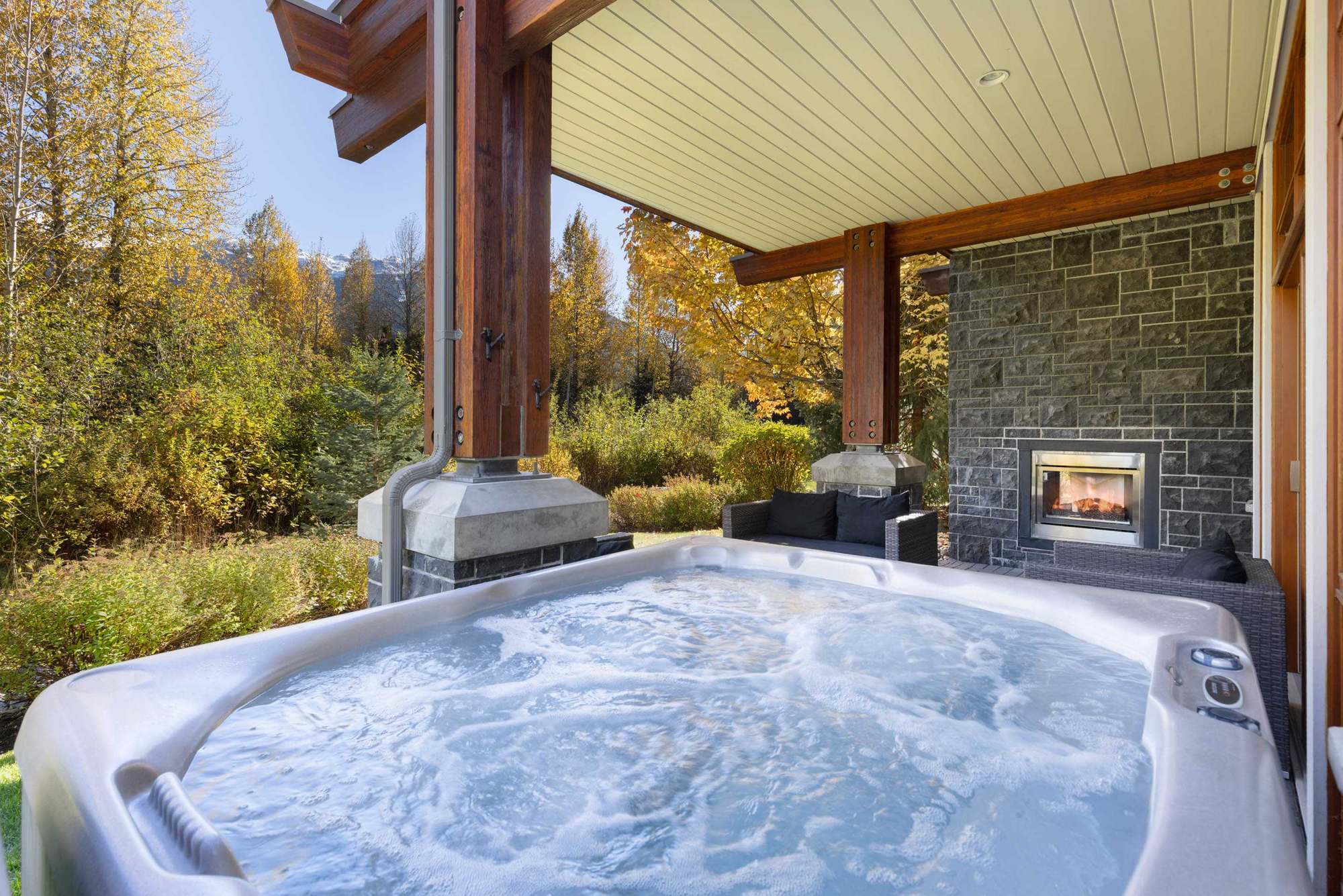 Covered patio with timber soffit, stone and an outdoor fireplace at Fitzsimmons Walk in Whistler, built by Burj Enterprises