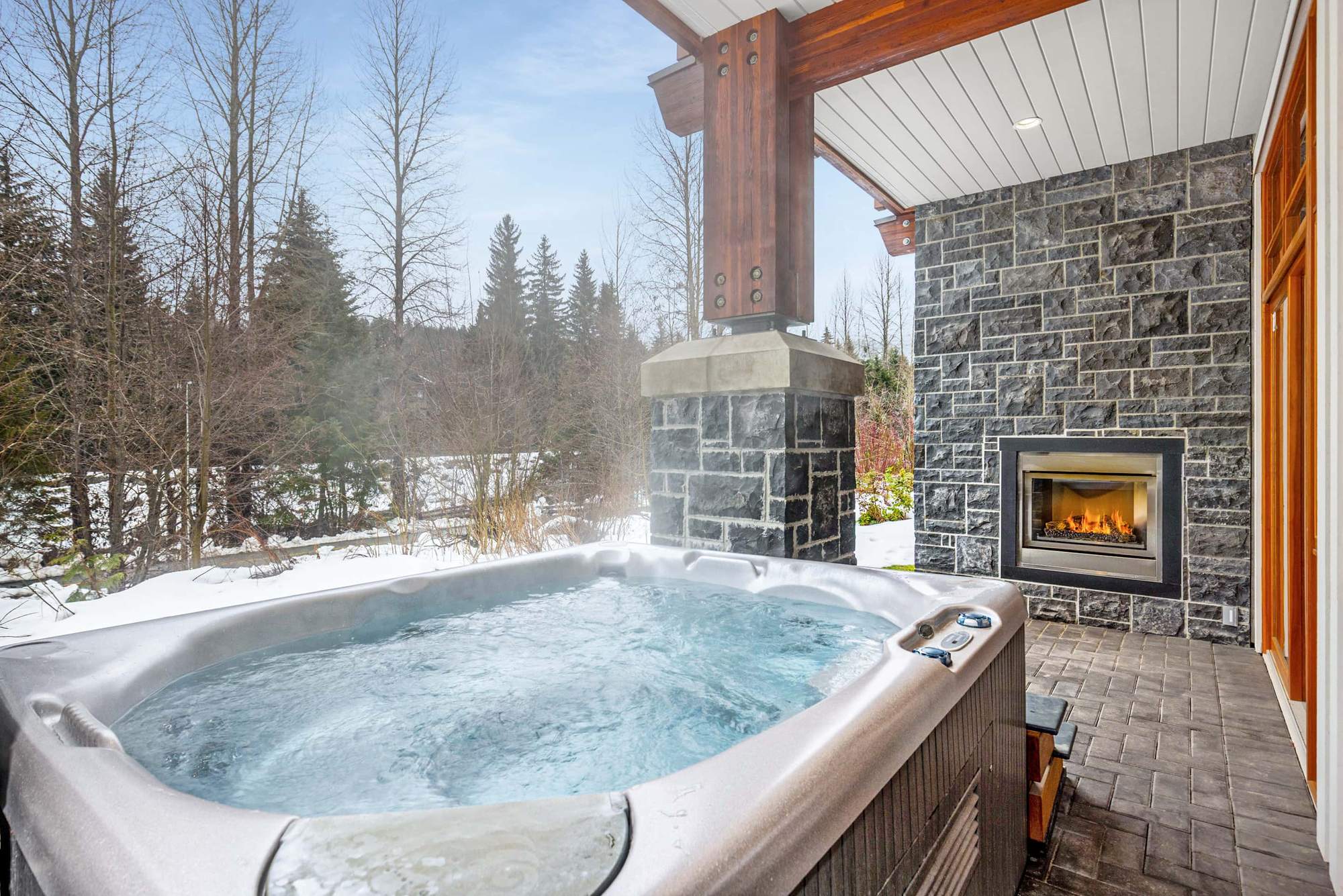 Fitzsimmons Walk in Whistler, a covered patio in winter carried on timber posts, with a stone chimney and a finished soffit above, built by Burj Enterprises