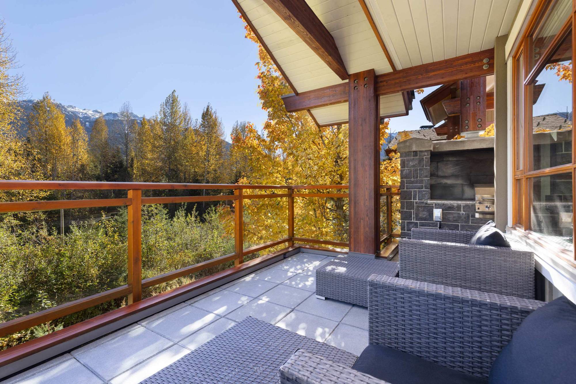 Fitzsimmons Walk in Whistler, a covered deck in autumn with a timber railing, a stone outdoor fireplace and a finished soffit overhead, built by Burj Enterprises