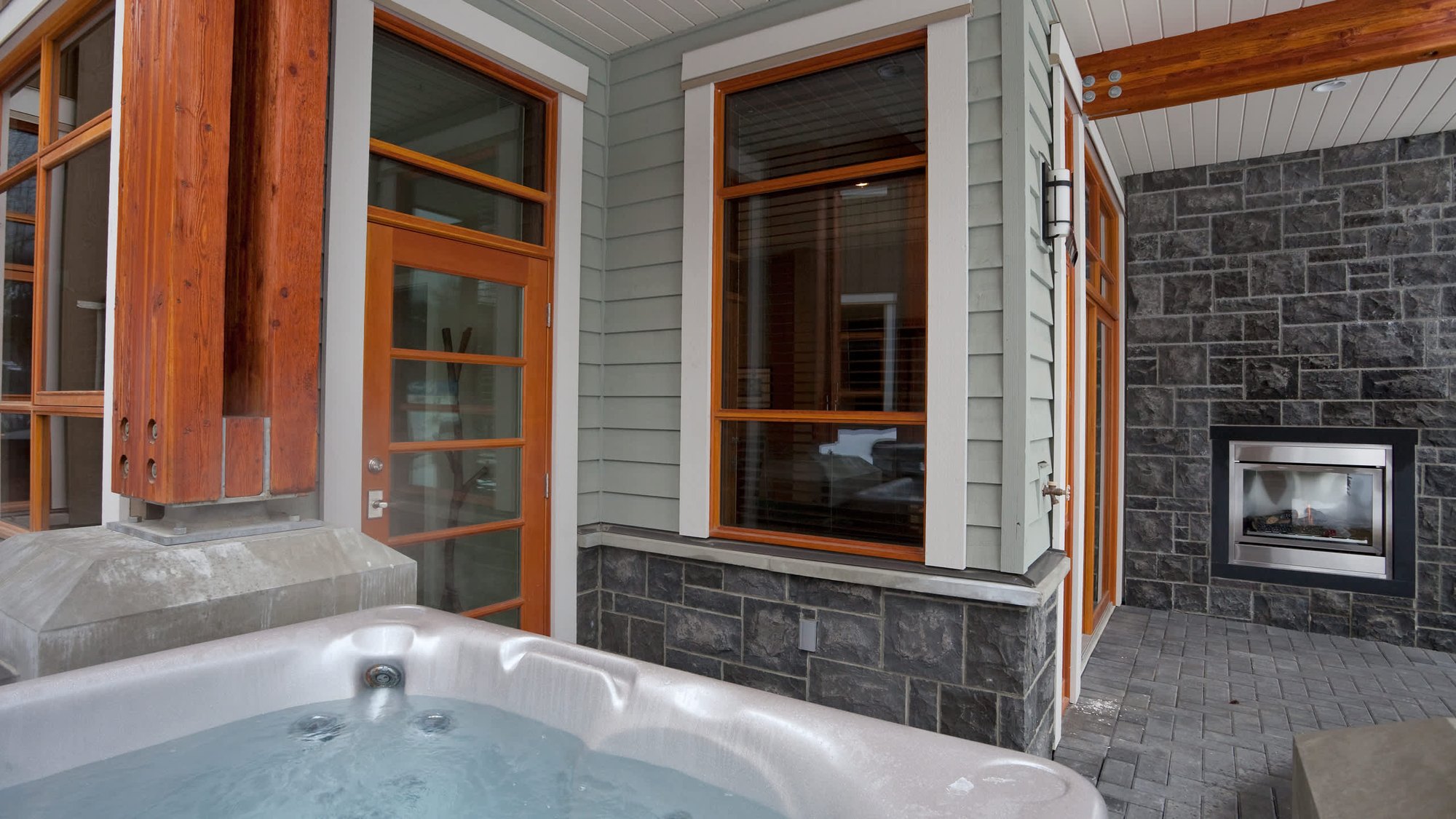 Fitzsimmons Walk in Whistler, a patio in siding and stone with timber trimmed windows under a lit soffit, built by Burj Enterprises