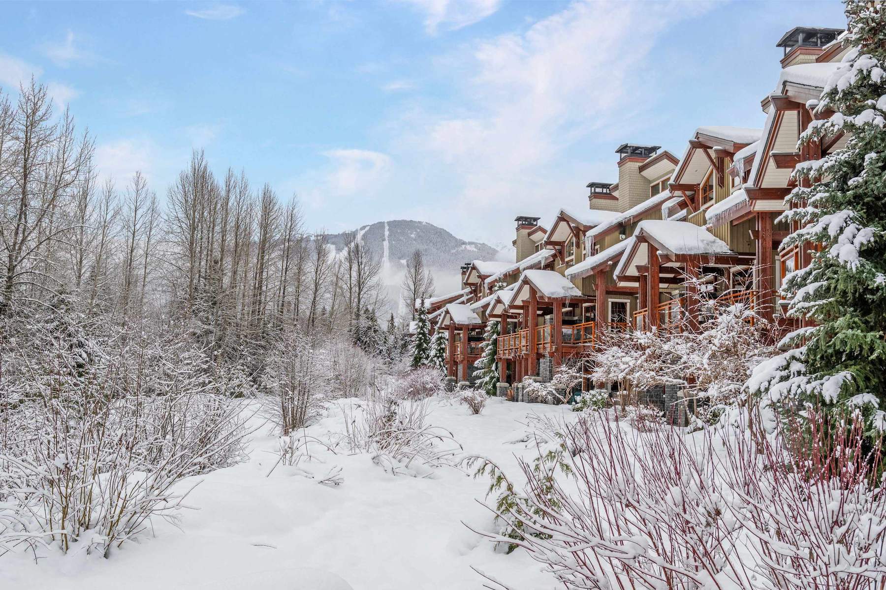 Fitzsimmons Walk in Whistler, a row of townhomes under fresh snow, gables, chimneys and shingle roofs across a winter clearing, built by Burj Enterprises