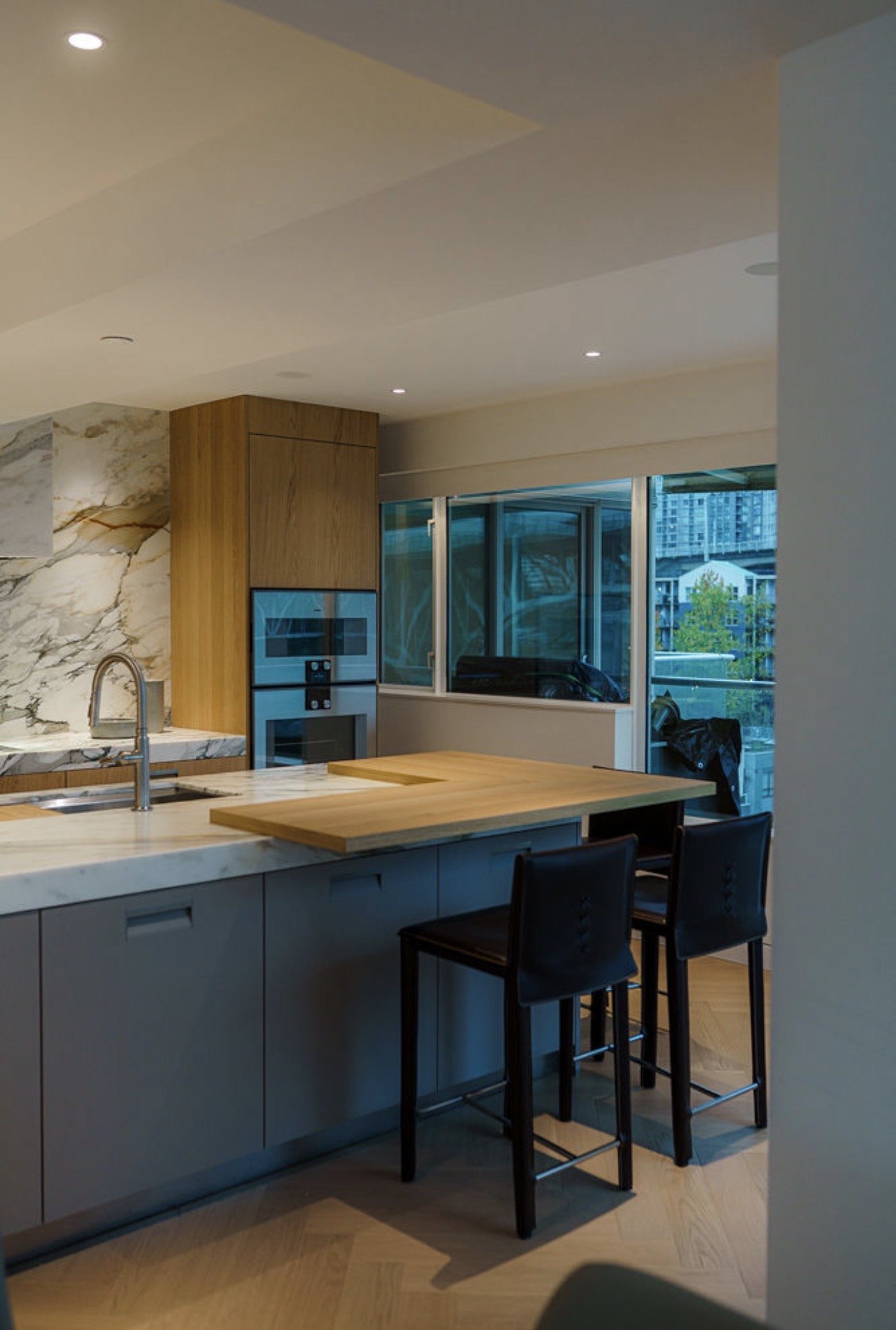 Kitchen island with a marble counter, oak upper cabinetry and a city window beyond, a residential renovation by Burj Enterprises